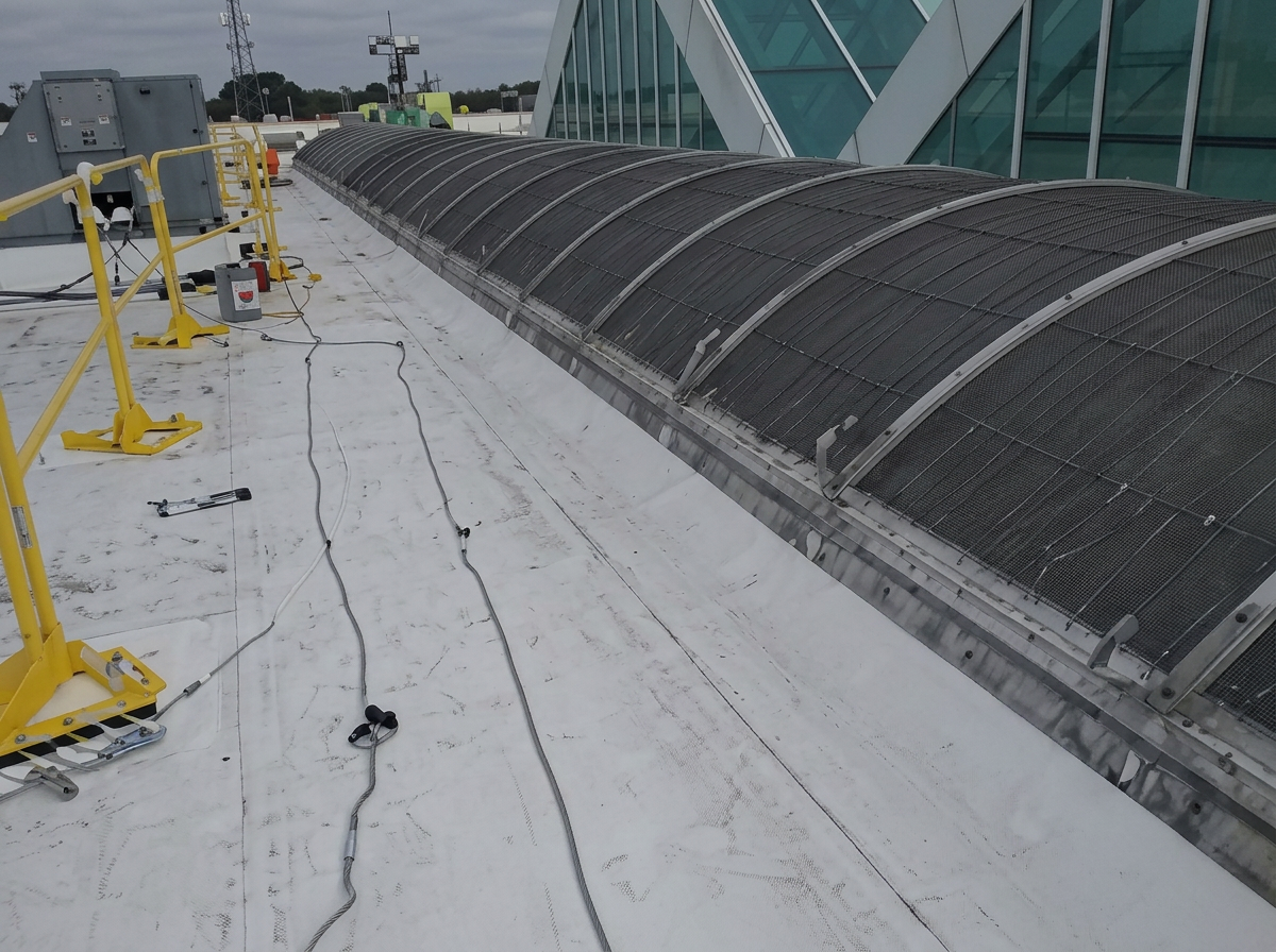 Commercial white membrane roof beside a long curved skylight structure with safety rails and lines