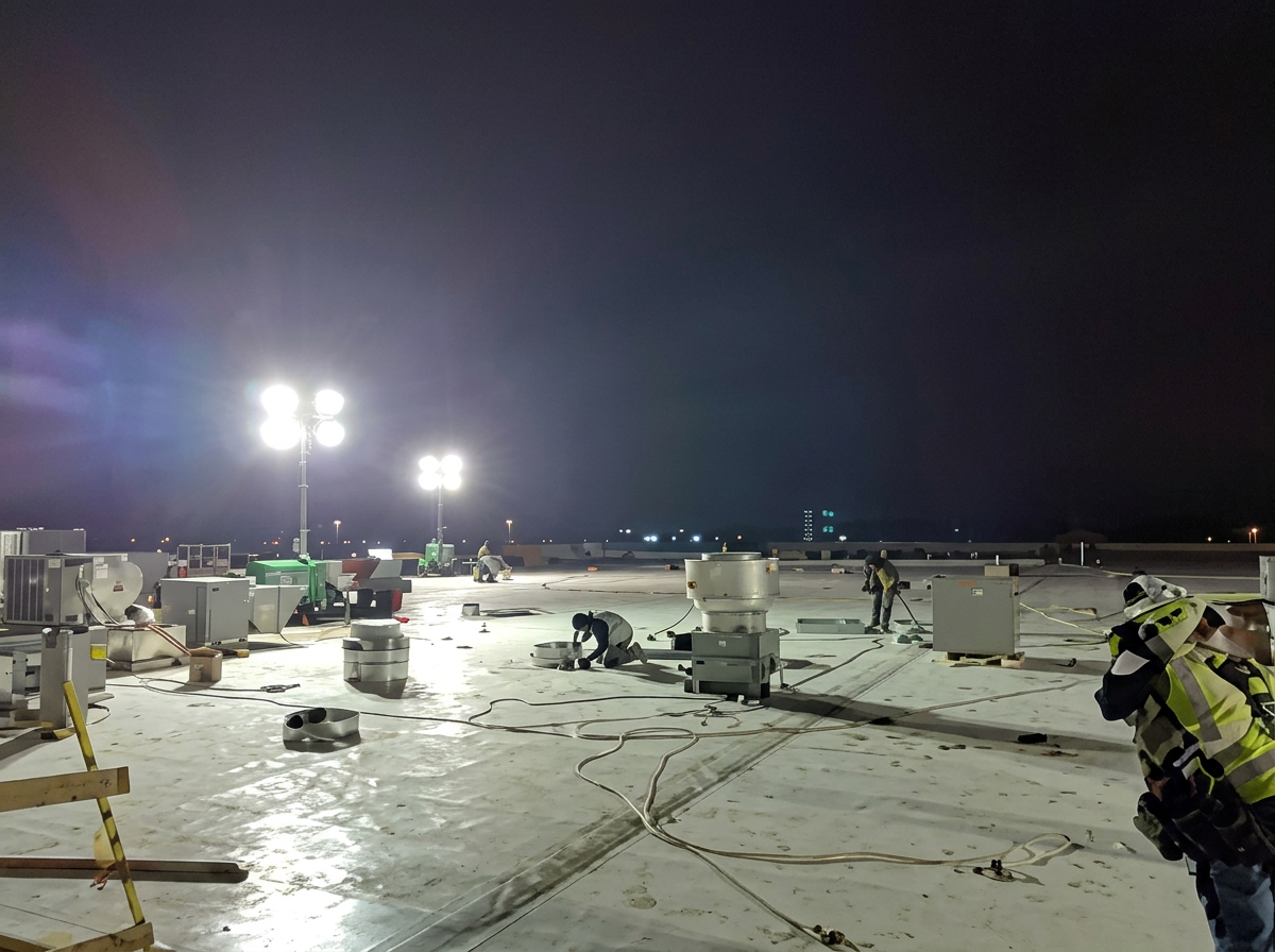 Nighttime commercial flat roof repair under bright work lights with crew across the roof deck